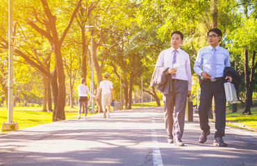 Obraz premium Businessman, They are walking on road in park. They are talking business. He is drinking coffee and His friend holding business bag. Photo concept business and relax time.