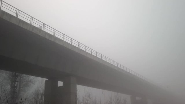 A large concrete bridge structure swallowed in fog.