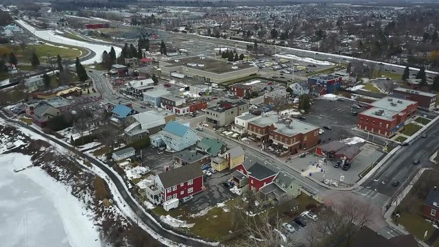 Cinematic aerial / drone footage descending over the lake with dry trees, snow, houses, a small town, cars in the background in Chambly, Quebec, Canada during winter season.