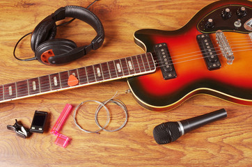 Electric guitar, microphone, headphones, strings on a wooden table.