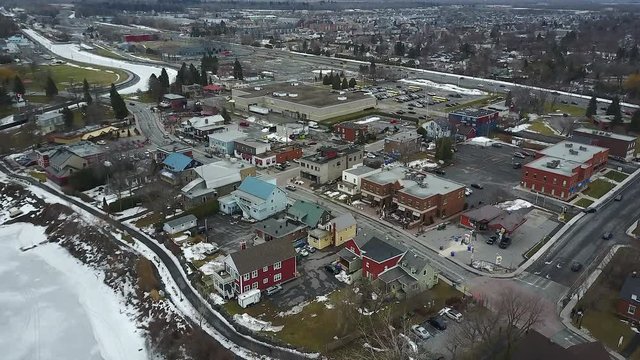 Cinematic aerial / drone footage descending over the lake with dry trees, snow, houses, a small town, cars in the background in Chambly, Quebec, Canada during winter season.