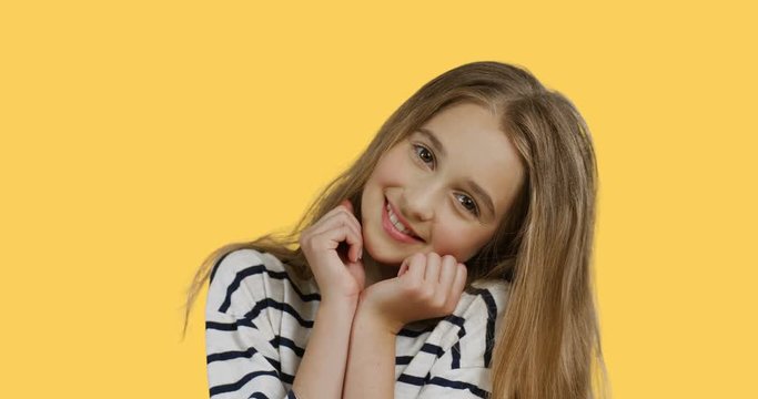 Portrait of the cute teen girl in the striped blouse smiling and posing in front of the camera. Yellow background.