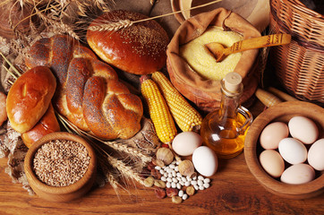 Baked bread, corn, eggs, flour, wheat grains on a wooden table.