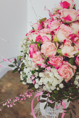 Cloe up view of a bouquet of pink roses and spring branches on white table against white wall