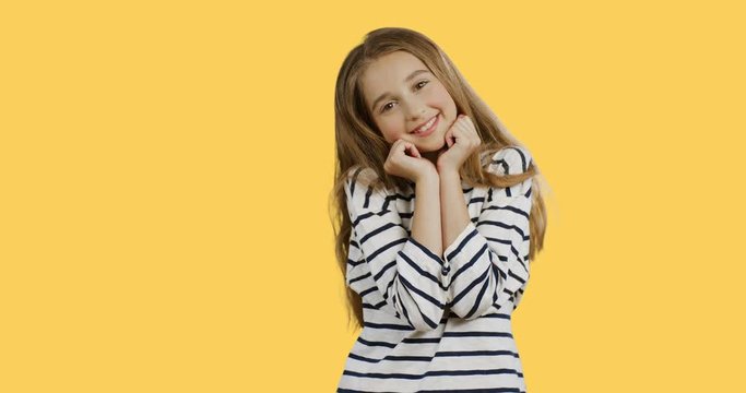 Portrait shot of the pretty nice teenage girl in the striped blouse smiling and posing in front of the camera on the yellow background.