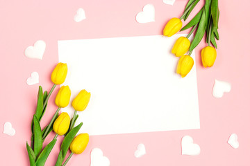 Blank white card with tulips flowers and hearts on pink pastel background. Flat lay, top view, copy space.