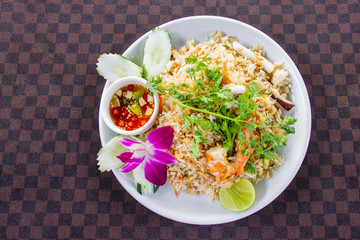 Fried rice with shrimp on the white ceramic dish decorated with orchid and hot spicy dipping sauce put on leather floor the grid pattern. Top view