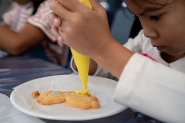 Cute asian child girl decorating cookies with fun
