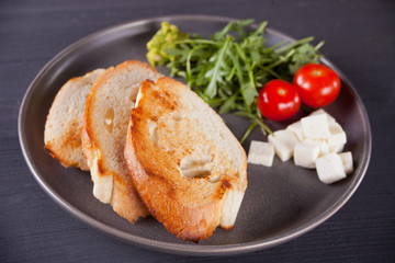 Sliced Toast Bread on black plate with tomatoes, feta and arugula