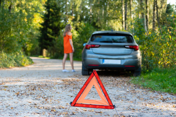 Stressful young woman driver hitchhikes and stops cars, asks for help as have problem with brocken car, uses red triangle sign to warn drivers about stop. (selective focus)