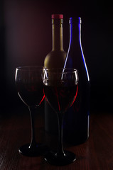 Two glasses of red wine and two bottles on dark