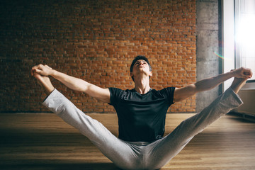 Young man doing yoga in big bright training gym