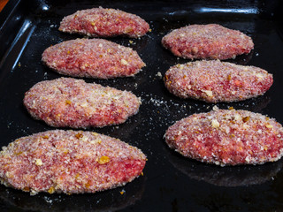 Meat patties semi-finished products, sprinkled with breadcrumbs, neatly spread on a baking sheet before cooking in the oven.