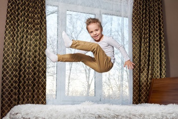 child fun home. Beautiful blond child 6 years old fooling around morning to room. Kid smiling jumping to bedroom on bed.