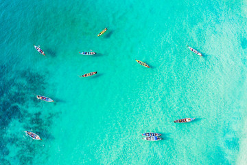 View from above, stunning aerial view of a large group of traditional longtail boats floating on a turquoise and clear sea that bathes the tropical Freedom beach in Phuket, Thailand.
