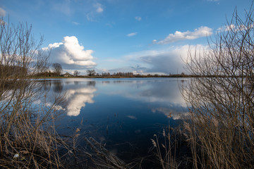 calm lake in bright sun light with reflections of clouds and trees and blue sky