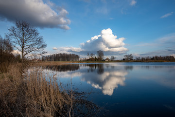 calm lake in bright sun light with reflections of clouds and trees and blue sky