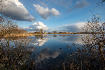 calm lake in bright sun light with reflections of clouds and trees and blue sky