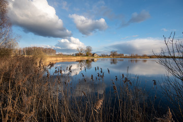 calm lake in bright sun light with reflections of clouds and trees and blue sky