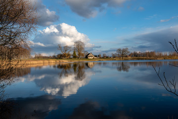 calm lake in bright sun light with reflections of clouds and trees and blue sky