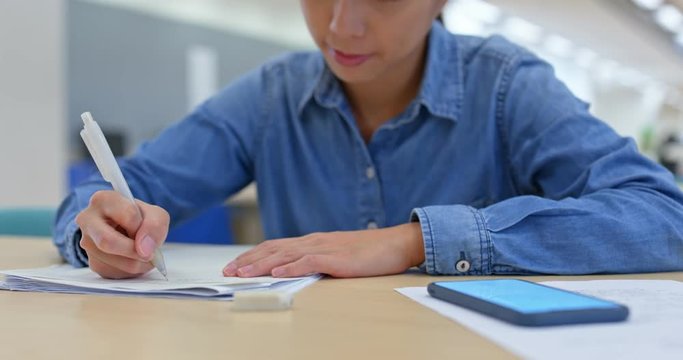 Woman work on the essay with using mobile phone in the library