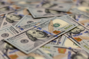 Macro shot of Benjamin Franklin's portrait on a new 100 dollar US money note, with defocused background of many more identical money notes in a mess.