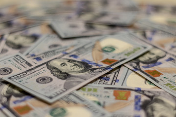 Macro shot of Benjamin Franklin's portrait on a new 100 dollar US money note, with defocused background of many more identical money notes in a mess.