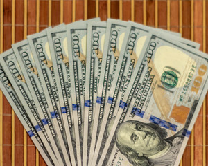 The stack is 100 dollar bills USD spread out like a fan, on a wooden background.