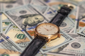 Wrist gold watch lie on the bills of 100 dollar money. Soft focus.