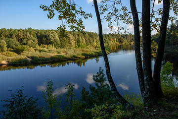 calm lake in bright sun light with reflections of clouds and trees and blue sky