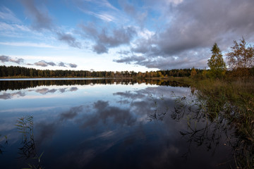 Obraz premium calm lake in bright sun light with reflections of clouds and trees and blue sky