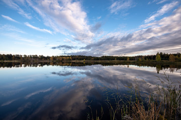 calm lake in bright sun light with reflections of clouds and trees and blue sky