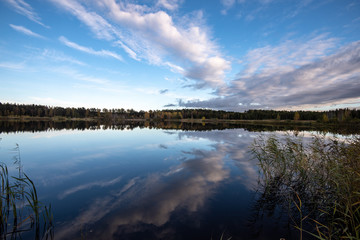 Fototapeta premium calm lake in bright sun light with reflections of clouds and trees and blue sky