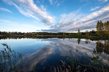 Obraz premium calm lake in bright sun light with reflections of clouds and trees and blue sky