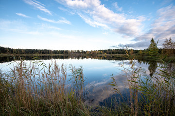 calm lake in bright sun light with reflections of clouds and trees and blue sky