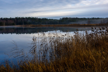 Obraz premium calm lake in bright sun light with reflections of clouds and trees and blue sky