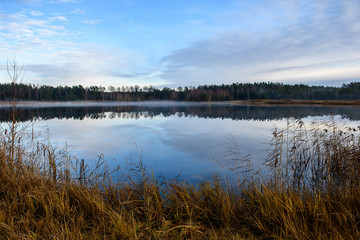calm lake in bright sun light with reflections of clouds and trees and blue sky