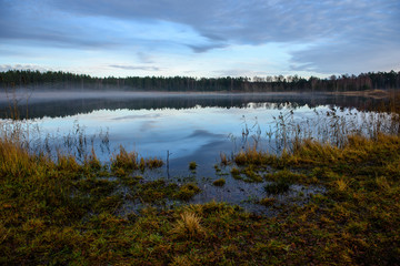 calm lake in bright sun light with reflections of clouds and trees and blue sky