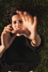 Portrait of an attractive young woman lying down on the grass touching the camera with her hands