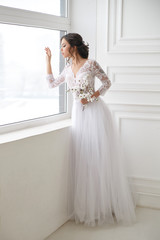 Portrait of a beautiful elegant bride waiting near a window in a bright interior.