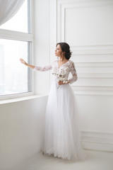 Portrait of a beautiful elegant bride waiting near a window in a bright interior.