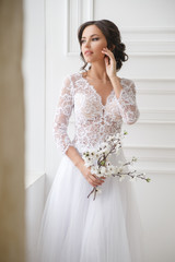Portrait of a beautiful elegant bride with a bouquet of sakura in a bright interior.