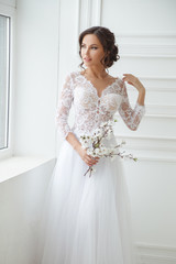 Portrait of a beautiful elegant bride with a bouquet of sakura in a bright interior.