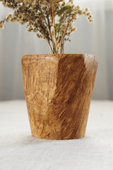 A wooden vase made of oak burl with dry yellow flowers standing on a white table cloth. Very unusual texture of the wood.