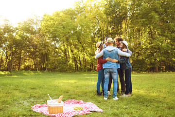 A group of friends stands embracing a picnic in the park.