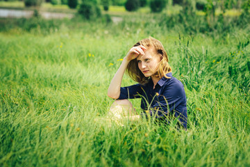 Portrait of a brooding girl in a meadow in the grass, sitting down for a walk on a Sunny day.