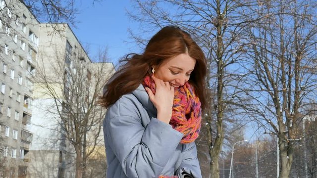 Close up portrait of smiling adult girl in blue coat and colorful knitted scarf during early spring time in the city