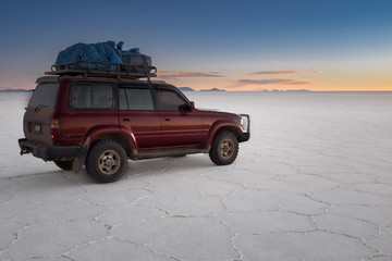 Fototapeta na wymiar A tour 4x4 car sits on the amazing white vast landscape of the largest salt plain in the world at Salar De Uyuni (Salt Flat), Bolivia with the cactus island in the distance