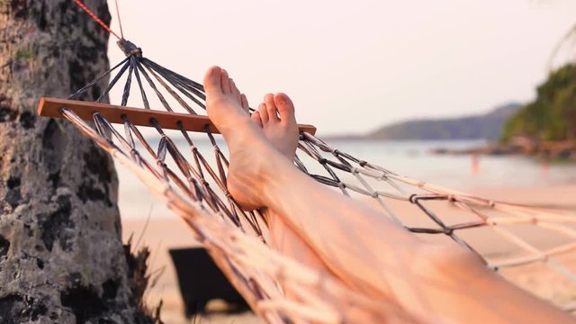 Woman relaxing in hammock by the beach at summer vacation holydays destination, swinging movement, close-up of legs, leisure and relaxation near the sea