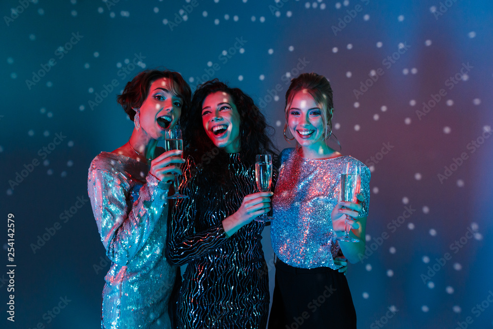 Wall mural Happy women posing isolated with disco ball lights holding glasses with champagne.